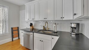 Una cocina con gabinetes blancos, encimera negra, pileta de acero inoxidable y cafetera.