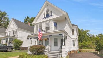 A two-story white house with a front porch, an American flag, and a mailbox.