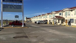 A motel with a signboard listing amenities like executive suites, full kitchens, air conditioning, fire places, cable TV, pool, and free breakfast. - Western Budget Plus Grande Prairie 2 (Grande Prairie)