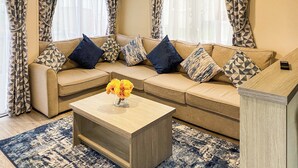 A living room with a beige sofa, patterned cushions, a wooden coffee table, and a blue and white patterned rug. - This lovely caravan is perfect for couples, friends, or families. (Sandown)