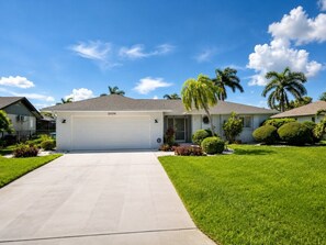 A residential house with a garage, a well-maintained lawn, and palm trees. - Coral Point with Heated Pool with Gulf Access (Cape Coral)