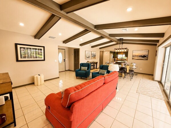 A spacious living area with a red sofa, blue armchairs, and a dining table. - Coral Point with Heated Pool with Gulf Access (Cape Coral)