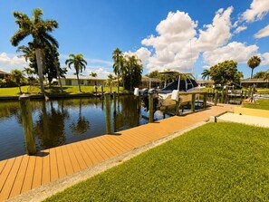 A marina with boats docked, a wooden dock, and palm trees. - Coral Point with Heated Pool with Gulf Access (Cape Coral)