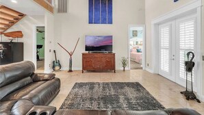 Un salón amplio con un sofá de cuero, un televisor de pantalla plana y un cuadro grande con palmeras.