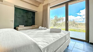 A modern hotel room with a large bed, a sofa, and a view of a vineyard through the glass doors. - Cozy home in Chiaramonte Gulfi (Chiaramonte Gulfi)