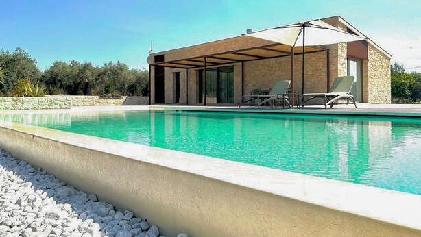 A modern pool area with a stone building, lounge chairs, and a clear blue pool. - Cozy home in Chiaramonte Gulfi (Chiaramonte Gulfi)