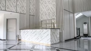 A modern lobby with a marble reception desk, a check-in counter, and a staircase leading to an upper level. - Helsinki Hotel Palu (South Palu)