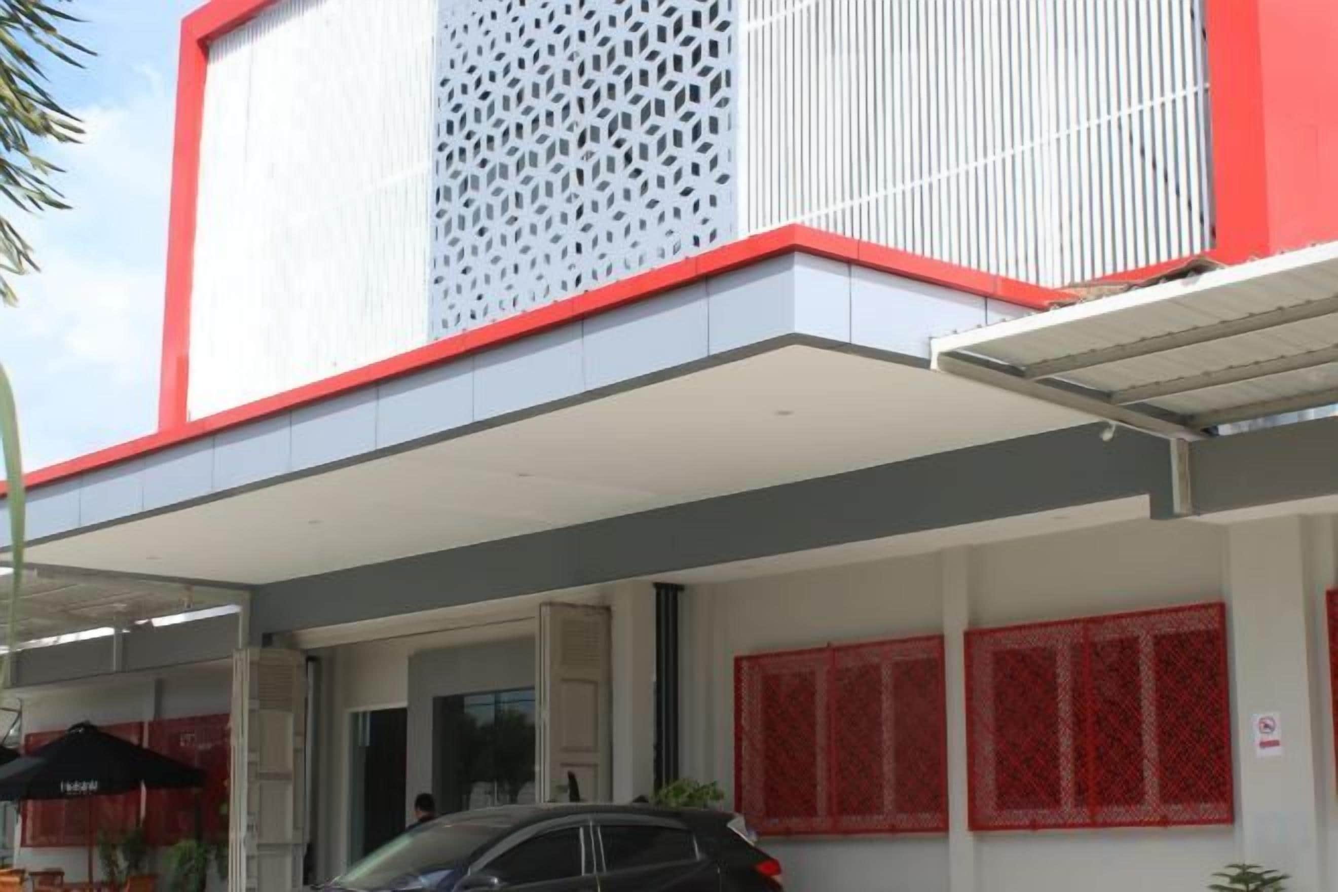 A building with a red and white facade, a covered entrance, and red patterned windows.