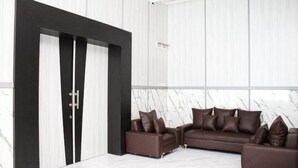 A modern living room with a sectional sofa, a black-framed door, and marble-patterned walls. - Helsinki Hotel Palu (South Palu)