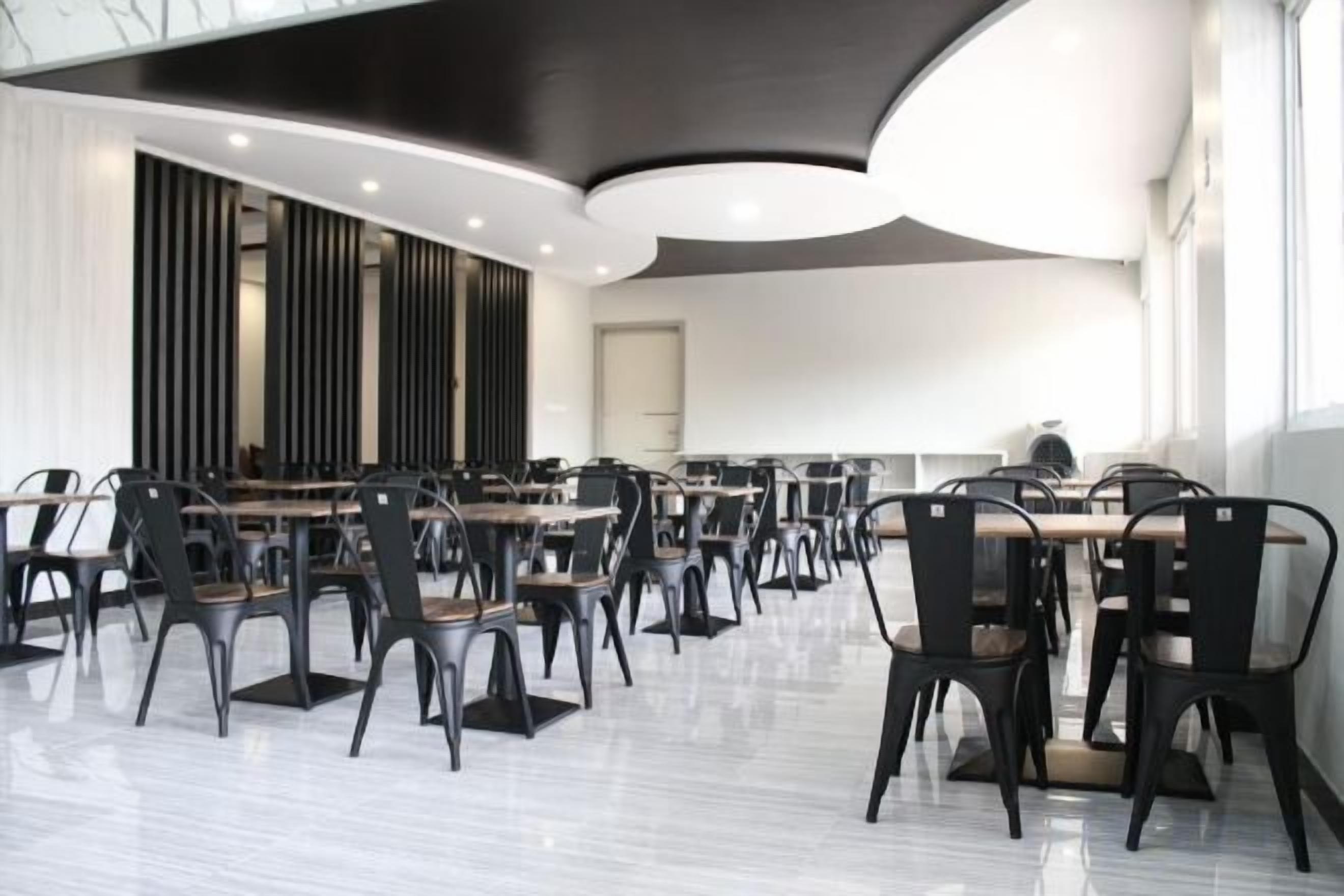 Un comedor moderno con varias mesas y sillas, techo curvo y ventanas amplias.