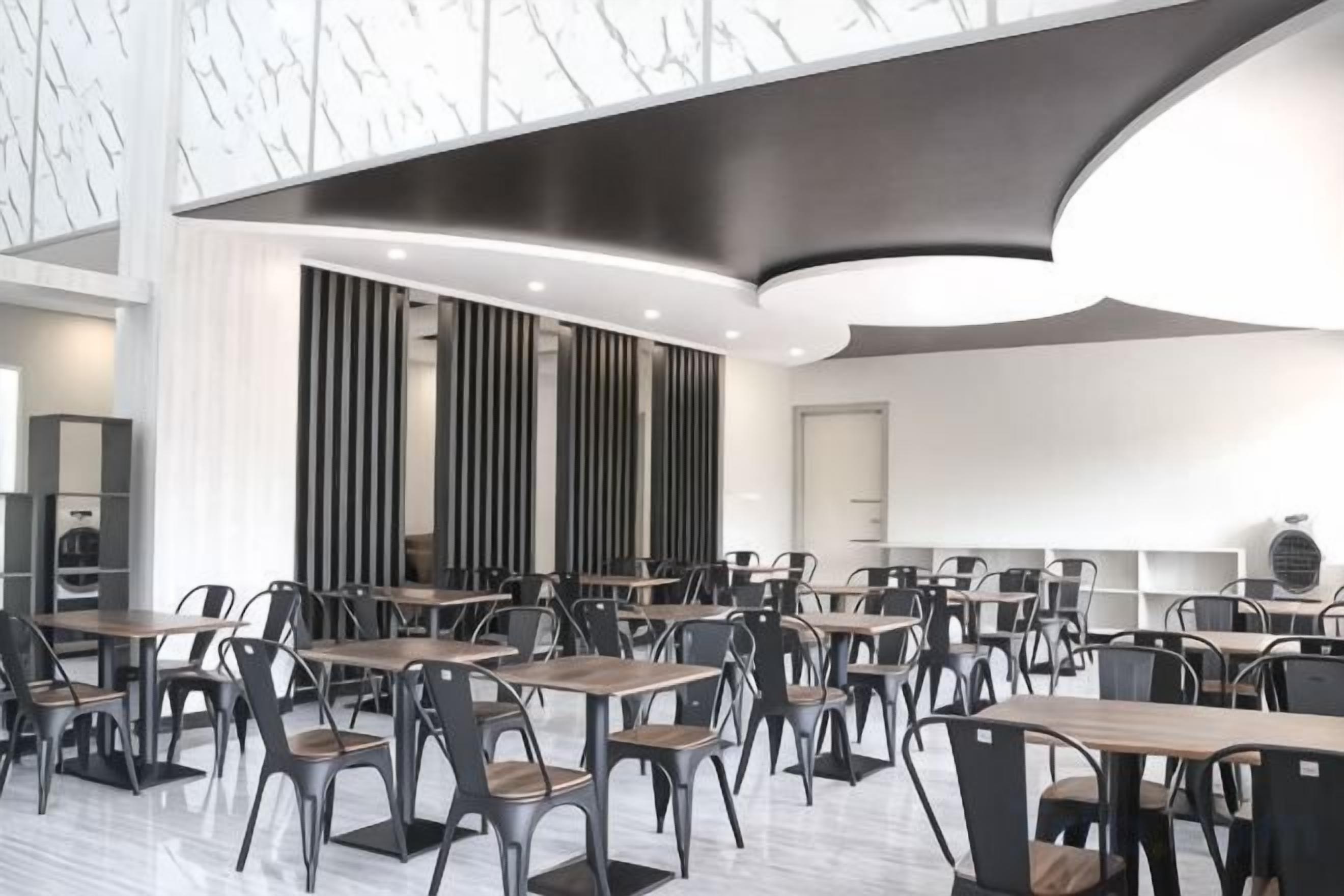 A modern dining area with multiple tables and chairs, a curved ceiling, and a large window.