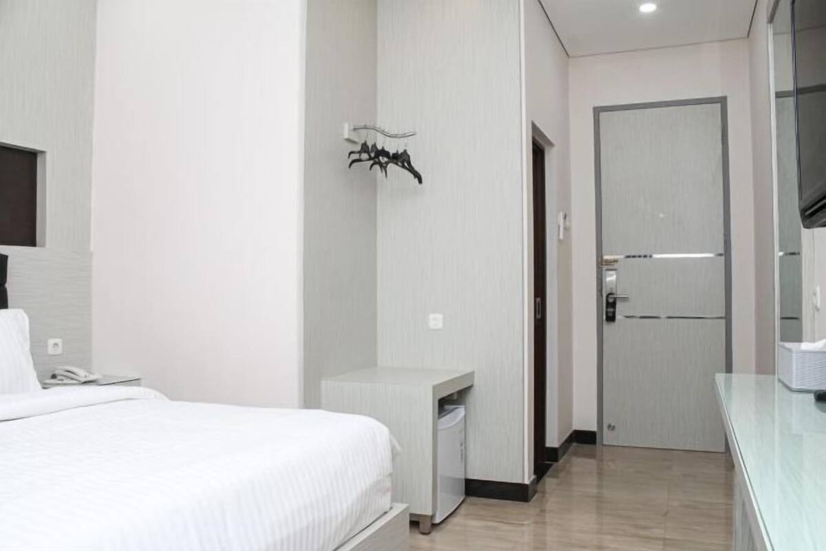 Ein Hotelzimmer mit Bett, Nachttisch, Kleiderschrank, Spiegel und einer Tür.