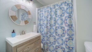 Un baño con un espejo redondo, un lavamanos y una cortina de ducha con estampado azul y blanco.