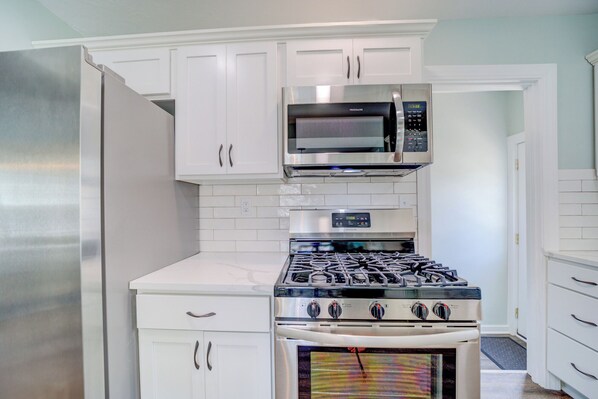 A kitchen with white cabinets, a stainless steel refrigerator, a microwave, a stove, and an oven. - Cute Cape Cod House! (Muskegon)