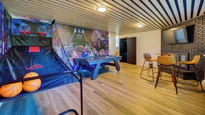 A room with a pool table, a basketball hoop, and a mural on the wall.
