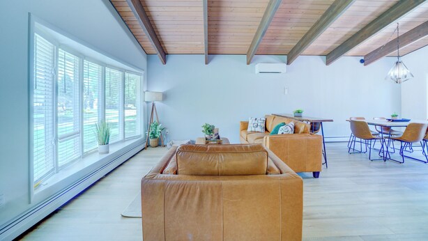 A spacious living area with a large window, a sofa, a dining table with chairs, and a hanging light fixture.