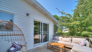 A covered outdoor deck with a sofa, a wooden table, and a wicker chair.