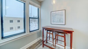 A corner room with two large windows, a wooden table, and a framed picture on the wall. - Lovely Mid-Century Modern - Apt B (Muskegon)
