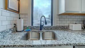 A kitchen with a double sink, a window with frosted glass, and a toaster on the counter. - Parisian Botanical - Apt D (Muskegon)