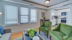 A living room with a sofa, a green armchair, and a coffee table with books and a vase of flowers. - Parisian Botanical - Apt D (Muskegon)