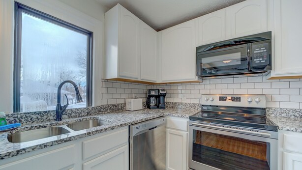 A kitchen with white cabinets, a stainless steel sink, a microwave, a coffee maker, and a double oven. - Parisian Botanical - Apt D (Muskegon)