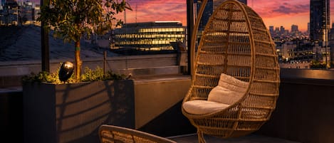Una terraza en la azotea con una silla colgante, una silla de mimbre y una planta en maceta.