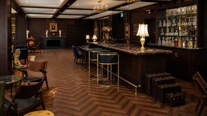 A bar area with a herringbone patterned floor, bar stools, a marble countertop, and a display of glassware. - Whisky Hotel  (Los Angeles)