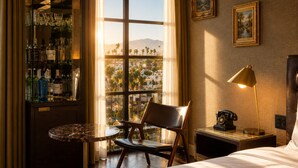 A hotel room with a large window, a bar area with bottles, a chair, a bedside table, a lamp, and a bed. - Whisky Hotel  (Los Angeles)