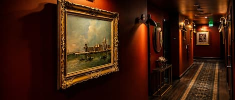 A hallway with a framed painting, wall-mounted lamps, and a patterned carpet.