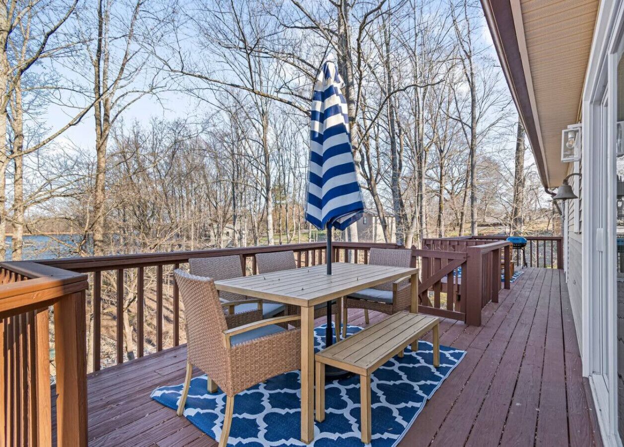 Une terrasse en bois avec une table et des chaises, un parasol suspendu, et une vue sur des arbres et un bâtiment.