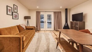 A living room with a sofa, a dining table, a TV, and a fireplace. - Slopeside Suite at Alyeska - Ski In Ski Out (Girdwood)