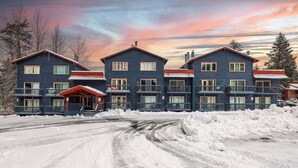 A multi-story building with a red roof and balconies, surrounded by snow. - Slopeside Suite at Alyeska - Ski In Ski Out (Girdwood)
