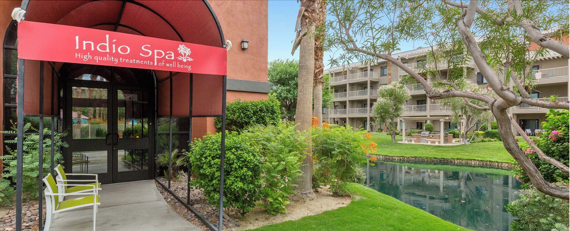 The entrance of Indio Spa with a sign, a pool, and surrounding greenery.