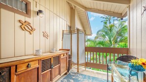 A room with a wooden cabinet, a glass table with a blue patterned rug, a chair, and a view of palm trees. - Chic Aloha Studio in Superb Princeville, w/AC & WiFi 
Explore Beautiful Napali! (Princeville)