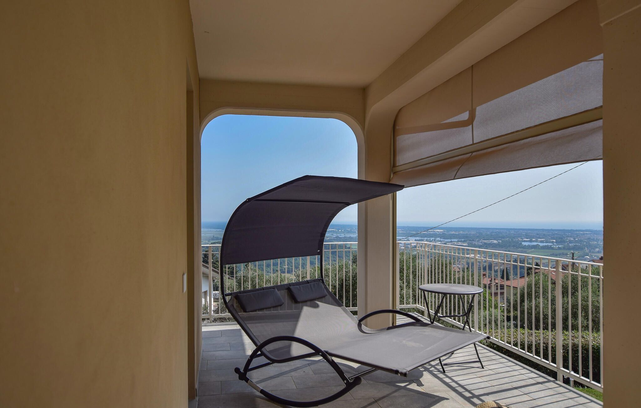 Ein Balkon mit Stuhl und Tisch, Blick auf eine Stadtlandschaft und ein klarer Himmel.