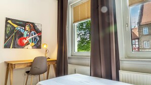 A hotel room with a bed, a desk with a chair, a lamp, and a painting on the wall.