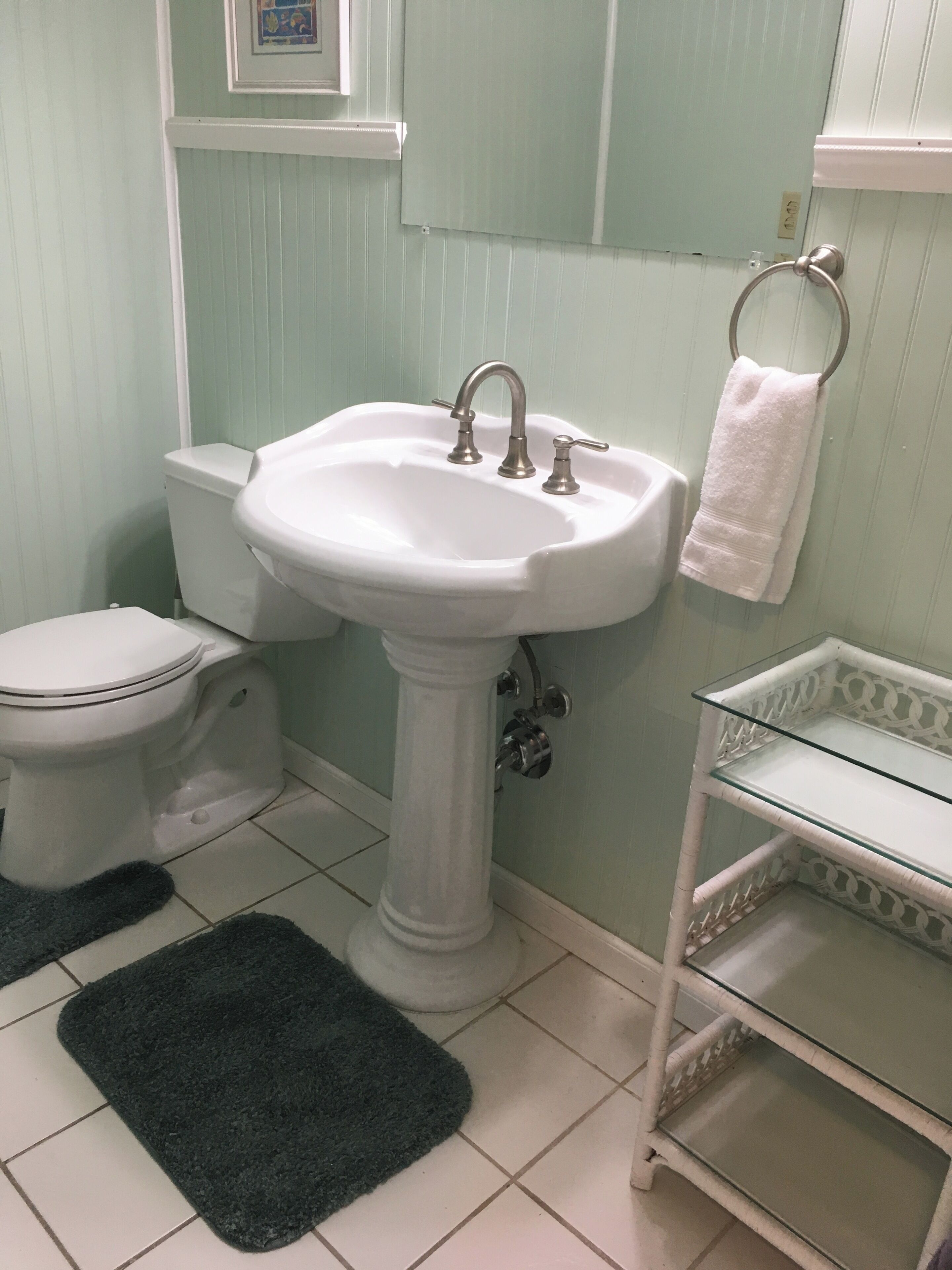 A bathroom with a pedestal sink, toilet, and a small glass shelf.