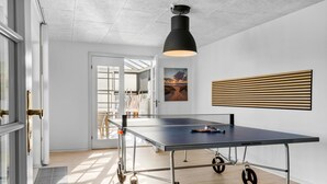 Et ping pong bord i et moderne rum med en loftlampe, et maleri og en væg beklædt med trælameller.