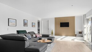 En moderne stue med en modulsofa, et sofabord og et fladskærms-TV monteret på en væg af træpaneler.