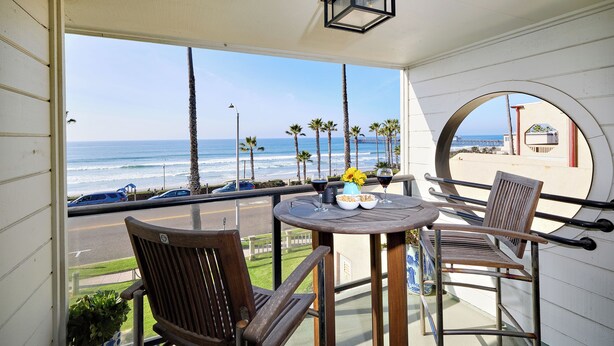 A balcony with a view of the ocean, a table with chairs, and a potted plant. - Coastal Luxury @ Tyson Park | Ocean Views & Private Balcony (Oceanside)