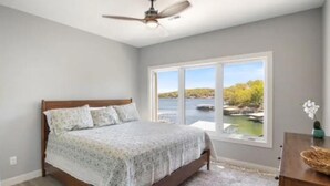 Ein Schlafzimmer mit einem Bett, einem Fenster mit Blick auf ein Gewässer und Bäume sowie einem Deckenventilator.