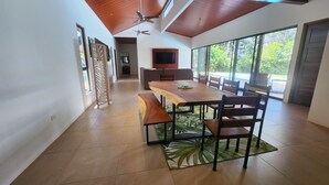 A spacious dining area with a long wooden table and benches, a ceiling fan, and large windows offering a view of greenery. - Spacious 3 bed, 3 bath home with breathtaking Mountain and Valley views. (Platanillo)