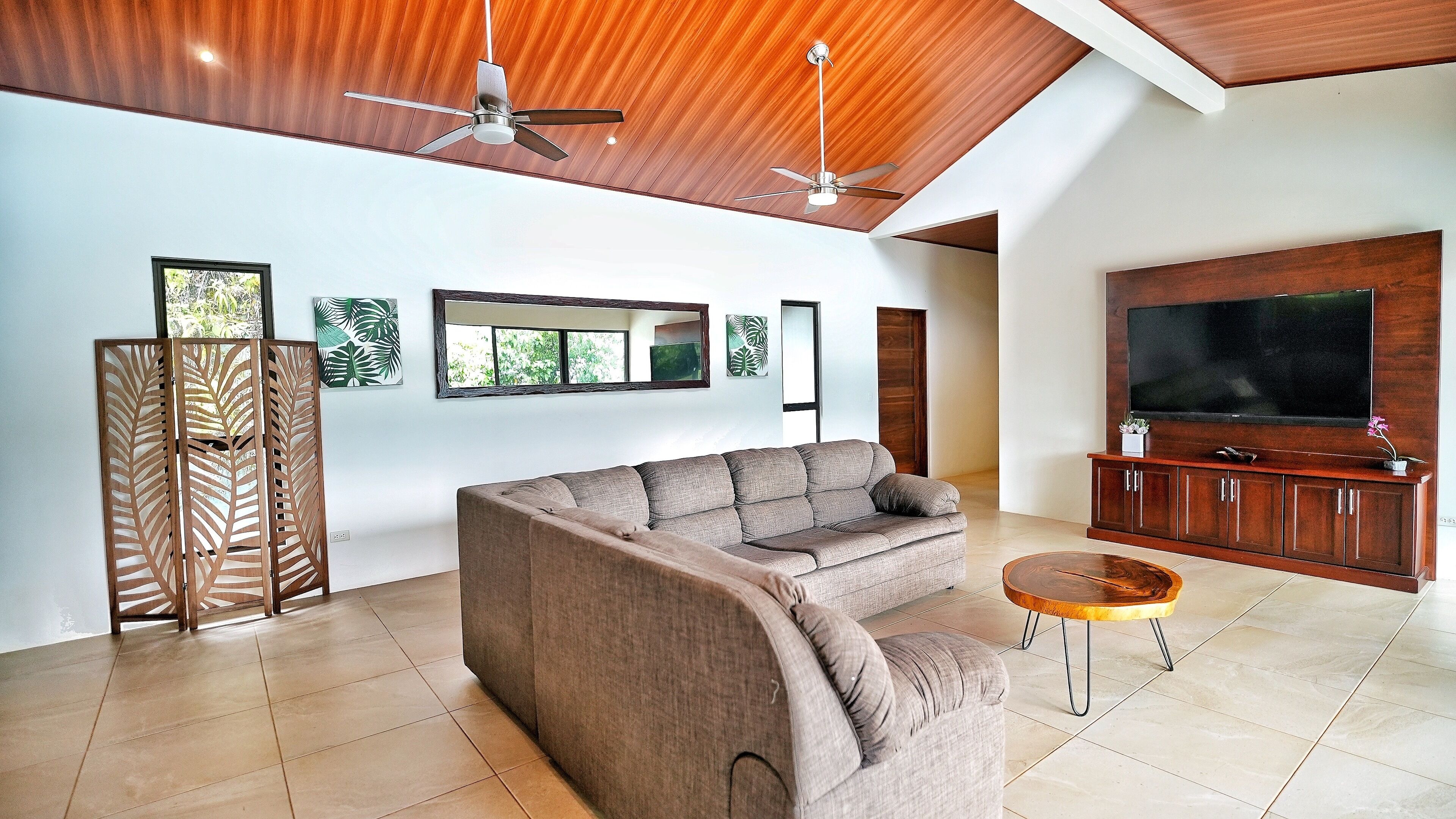 Ein modernes Wohnzimmer mit einer Couch, einem Couchtisch, einem Fernseher und Deckenventilatoren.