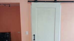 Una habitación con una puerta blanca, un electrodoméstico negro y un sofá gris.