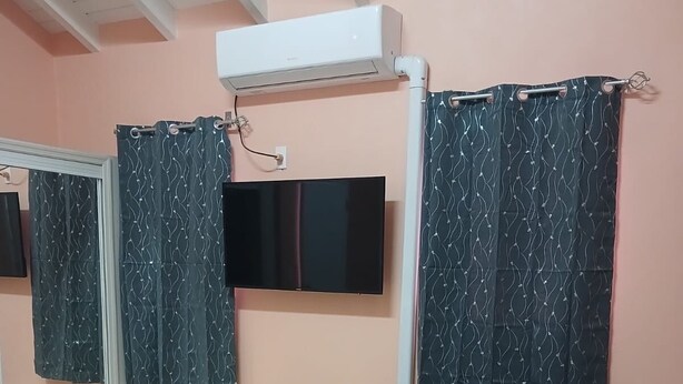 Una habitación con un espejo grande, un televisor de pantalla plana en la pared, dos sillas y un ventilador de techo.