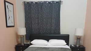 Un dormitorio con una cama, dos mesitas de noche, una cortina instalada en la pared y un cuadro enmarco.