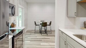 A modern kitchen with a dining area, featuring a central island with chairs, a built-in oven, and a large window providing natural light. - Cozy Mountain Hideaway, Next to Hiking Trails & Waterfalls! (Highlands)