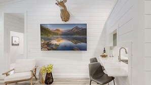 A modern kitchen with white cabinetry, a mounted deer head, and a large landscape painting. - Cozy Mountain Hideaway, Next to Hiking Trails & Waterfalls! (Highlands)