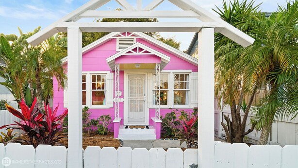 A pink house with a white porch and a picket fence.