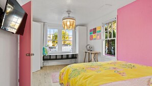 A bedroom with a bed, a window seat, a fan, and a chandelier.